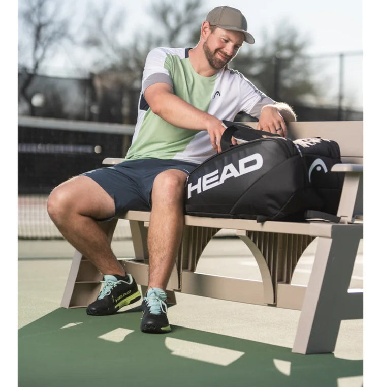 Jugador de pickleball sentado en un banco con la bolsa Radach Sports HEAD PRO negra y blanca en una pista exterior