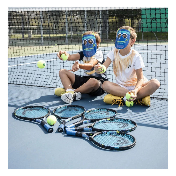 Dos niños con máscaras de Radach Sports jugando con raquetas de tenis Head Novak 25 Junior en una pista de tenis