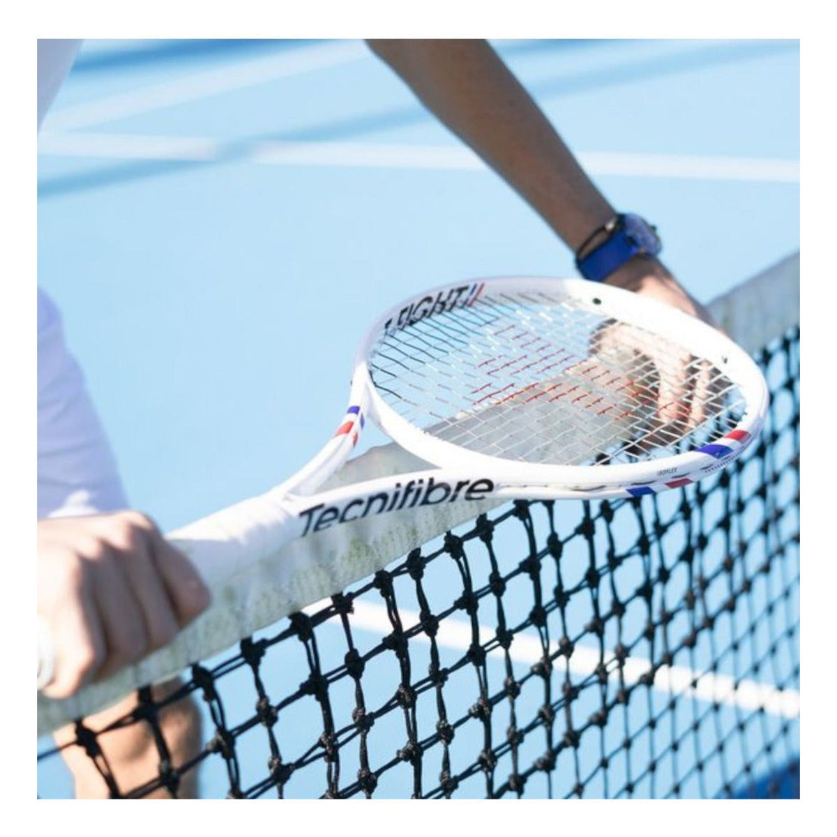 Raqueta de tenis Tecnifibre T-Fight 255g blanca con detalles en azul y rojo, sostenida en una red por Radach Sports.